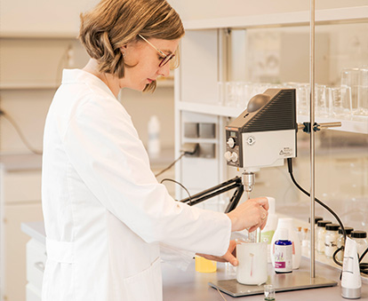Jasmin in a white lab coat works with a stirrer in the laboratory.